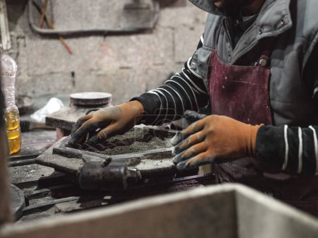Téléchargez les photos : Cultivez un travailleur masculin méconnaissable dans un tablier et des gants de protection travaillant avec un moule en métal tout en préparant du matériel pour la fabrication de carreaux à l'usine - en image libre de droit