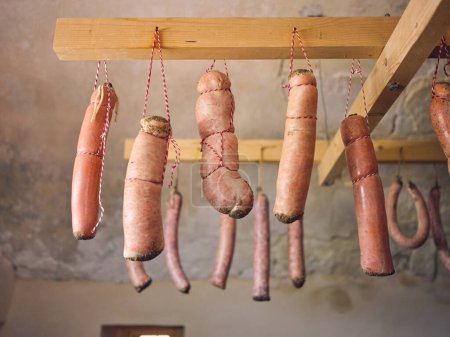 Foto de Desde abajo de conjunto de embutidos caseros en tripas de cerdo atadas con cordones culinarios colgando sobre vigas de madera para secar en Matanza en Mallorca - Imagen libre de derechos