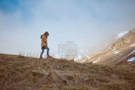 Photo for Full body side view of boy in warm clothes strolling on grassy field near mountain slope with hoarfrost in nature - Royalty Free Image