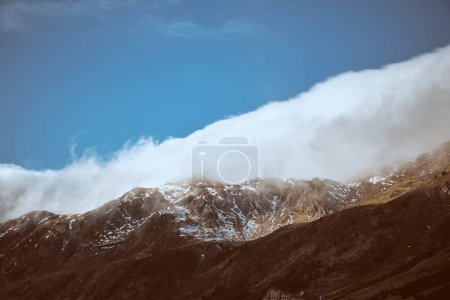 Foto de Terreno de montaña áspero cubierto de heladas blancas ubicadas contra el cielo azul con densas nubes blancas en el día soleado en la naturaleza - Imagen libre de derechos