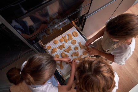 Foto de Desde arriba de niños anónimos poniendo galletas dulces crudas con diferentes formas en bandeja para hornear mientras preparan pasteles en el horno - Imagen libre de derechos