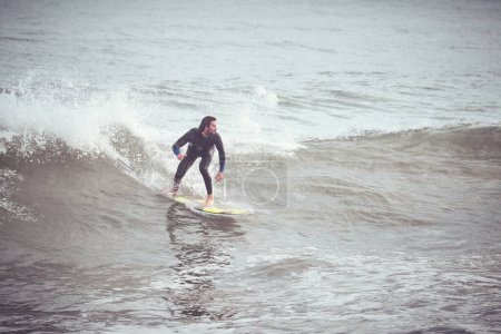 Foto de Desde arriba de cuerpo completo surfista masculino en traje de neopreno de pie en la tabla de surf y montar en ola y mirando hacia adelante en el océano - Imagen libre de derechos