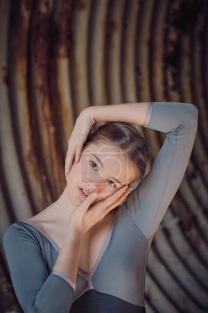 Foto de Encantadora joven bailarina tocando tiernamente la cabeza y mirando hacia otro lado mientras baila ballet en un viejo túnel abandonado con paredes oxidadas - Imagen libre de derechos
