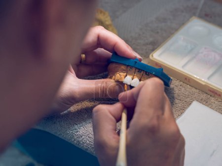 Foto de Desde arriba de la cosecha ortodoncista masculino poner cerámica con cepillo en la prótesis dental mientras se hace prótesis de mandíbula - Imagen libre de derechos