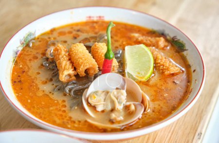 Photo for High angle of appetizing hot soup with soba noodles served with rolls of crispy chicken skin with lime slice and mussels with red pepper - Royalty Free Image