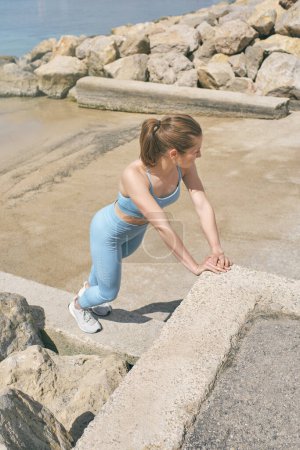 Photo for From above side view of female athlete in sportswear leaning with hands on stone fence while warming up and looking away - Royalty Free Image