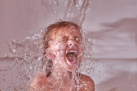 Photo for Boy with closed eyes shouting loudly while sitting in bathtub under stream of clear water during bath procedure at home - Royalty Free Image