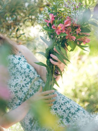 Photo for Faceless unrecognizable woman in dress holding creative bouquet of fresh flowers while standing in green garden in daylight - Royalty Free Image