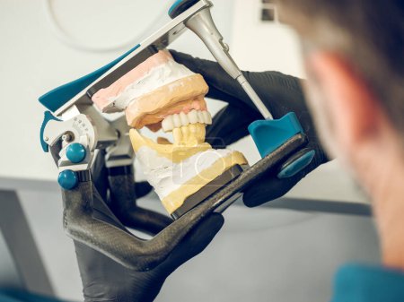 Foto de Vista posterior del dentista borroso irreconocible en guantes que sostienen el instrumento mientras trabaja en la mandíbula durante las prótesis dentales - Imagen libre de derechos
