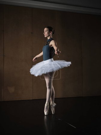 Photo for Side view of full body slender ballerina in tutu balancing on tiptoes in pointe shoes and dancing in studio - Royalty Free Image