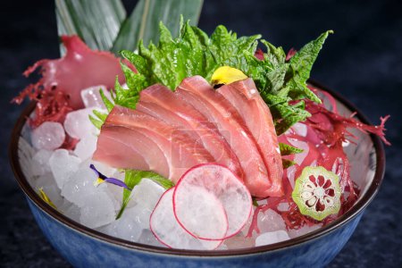 Foto de Cuenco con delicioso sashimi con filete de pescado fresco y rábano y lima colocados en el hielo decorado con hojas de plátano - Imagen libre de derechos