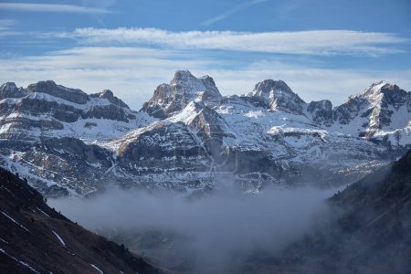 Téléchargez les photos : Brume épaisse couvrant la vallée contre la chaîne de montagnes enneigées et ciel bleu nuageux par une journée d'hiver ensoleillée dans la nature - en image libre de droit