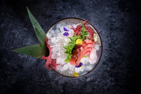 Photo for Bowl with yummy sashimi with fresh fish fillet and radish and lime placed on ice decorated with banana leaves - Royalty Free Image