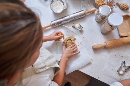 Téléchargez les photos : D'en haut de la récolte enfant méconnaissable faire des biscuits faits maison avec coupe de la pâte déployée sur la table - en image libre de droit
