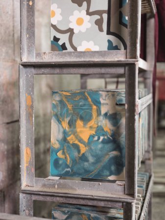 Foto de Azulejos artesanales de cerámica vidriada multicolor creativa con adorno abstracto colocado en filas en estantes de metal en taller artesanal - Imagen libre de derechos