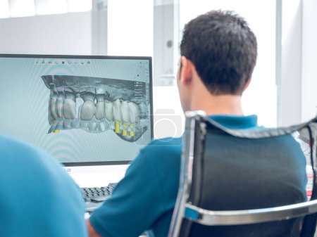 Téléchargez les photos : Vue arrière d'un technicien dentaire méconnaissable assis sur une chaise dans une clinique moderne et regardant le modèle numérique 3D des dents exposées - en image libre de droit