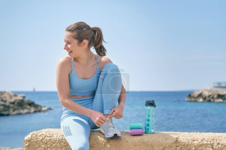 Photo for Young content female athlete in sportswear having break from workout while looking away against ocean - Royalty Free Image