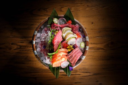 Photo for Top view of tasty healthy sashimi with vegetables and herbs served in bowl on wooden table with slice of fresh salmon and radish and lime - Royalty Free Image