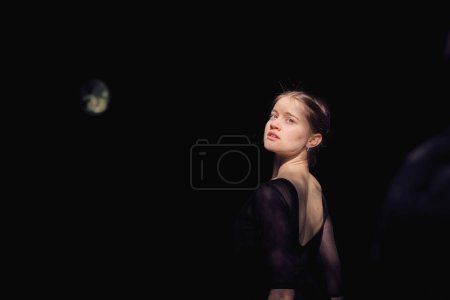 Téléchargez les photos : Vue de dos de la danseuse de ballet tendre debout contre l'obscurité dans la nature par une journée ensoleillée et regardant par-dessus l'épaule - en image libre de droit