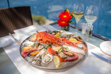 Téléchargez les photos : Spectaculaire homard aux moules, crevettes, palourdes et palourdes rasées présenté sur une assiette avec glace. Avec vue spectaculaire sur la mer à Majorque. - en image libre de droit