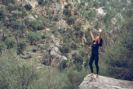 Photo for Excited barefoot woman raising arms and yelling while standing on boulder near mountain ridge and enjoying freedom during trip in Mallorca, Spain - Royalty Free Image
