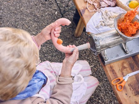 Photo for High angle of elderly unrecognizable female worker stuffing intestine from mincer on table in countryside - Royalty Free Image
