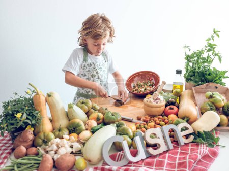 Photo for Focused adorable preteen boy in apron cutting fresh ripe vegetables on chopping board while preparing healthy food of raw ingredients - Royalty Free Image