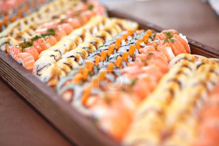 Foto de Surtido de apetitosos rollos con pescado servido en bandeja de madera en la mesa en el restaurante asiático - Imagen libre de derechos