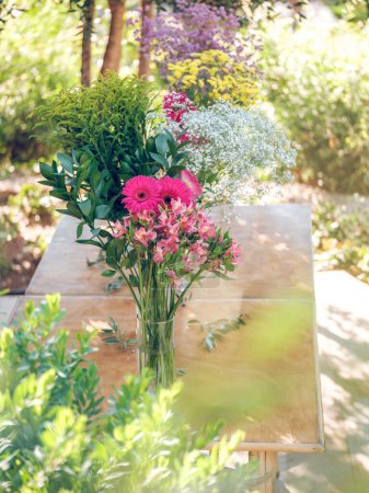 Téléchargez les photos : Diverses fleurs fraîches multicolores en fleurs dans des vases en verre placés sur une table en bois sur fond flou de jardin - en image libre de droit