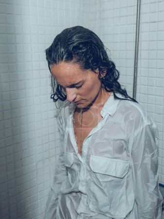Téléchargez les photos : Femme fatiguée en chemise blanche et avec les cheveux mouillés échouage avec les yeux fermés et la tête tombante sous pulvérisation d'eau dans la cabine de douche et de détente - en image libre de droit