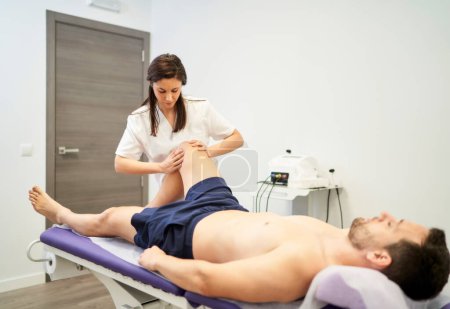 Téléchargez les photos : Un homme recevant un traitement du genou au cabinet du physiothérapeute - en image libre de droit