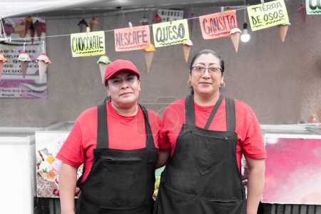 Photo for Portrait of two Hispanic adult women posing in front of their ice cream market stall. Concept of traditional Mexican dessert - Royalty Free Image