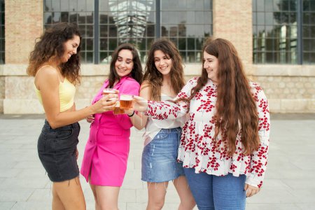 Photo for Young women friends toasting with a beer and smiling with joy as they celebrate their reunion - Royalty Free Image