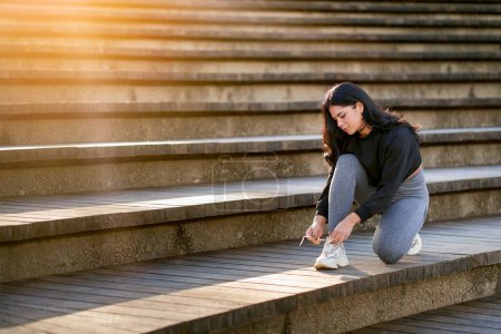 Téléchargez les photos : Jeune femme brune attacher ses chaussures se préparer à jouer exercice - en image libre de droit