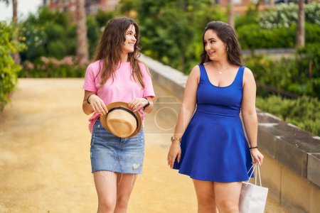 Foto de Dos amigas jóvenes pasean por un parque mirándose y hablando - Imagen libre de derechos