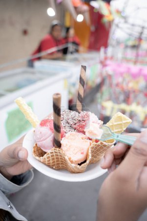 Photo for A young Hispanic woman is eating a traditional ice cream in front of a street market stall. Concept of traditional Mexican dessert - Royalty Free Image