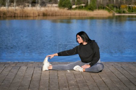 Foto de Una joven deportista se estira mientras está sentada en un embarcadero del lago - Imagen libre de derechos