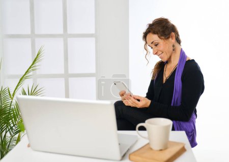 Téléchargez les photos : Une femme travaillant avec un ordinateur portable répond au téléphone à la maison - en image libre de droit