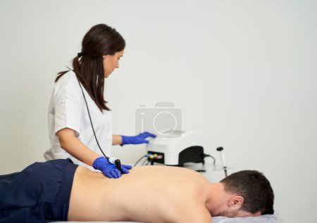 Téléchargez les photos : Une physiothérapeute qui donne un traitement de diathermie sur le dos du patient. - en image libre de droit