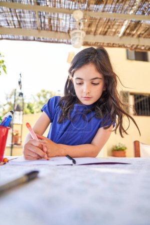 Foto de Chica hispana preadolescente con cabello oscuro en ropa casual sentada a la mesa y dibujo con marcadores de colores en el patio trasero - Imagen libre de derechos