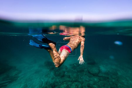 Téléchargez les photos : Enfant sans visage en palmes plongeant et nageant dans de l'eau de mer turquoise transparente et propre - en image libre de droit