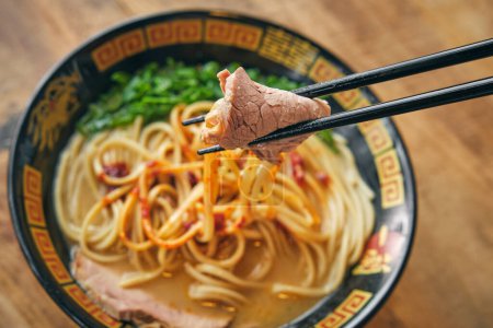Photo for Bowl of yummy Japanese noodle soup with chopped scallions under meat slice between chopsticks - Royalty Free Image