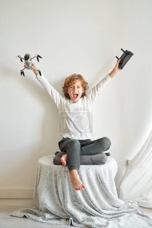 Photo for Full body of barefoot happy preteen boy screaming joyfully and raising hands happily while rejoicing presented drone with remote control - Royalty Free Image