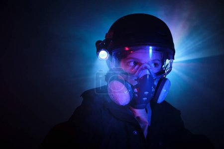 Photo for Robber in protective respirator with shining flashlight observing territory while standing in dark mint with glowing blue lights during illegal heist - Royalty Free Image