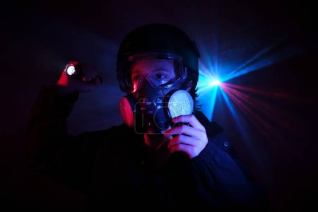 Photo for Boy in protective respirator shining with bright flashlight and looking away while standing in dark mint with glowing illumination during heist - Royalty Free Image