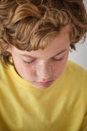 Téléchargez les photos : Cultiver enfant triste dans des vêtements jaunes avec des taches de rousseur sur la peau du visage et les cheveux ondulés - en image libre de droit