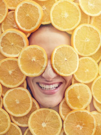 Photo for Overhead of lady smiling happily in lot of cut fresh oranges with pieces covering eyes - Royalty Free Image