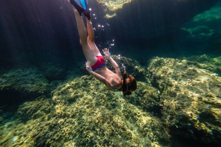 Foto de Cuerpo completo de adolescente en máscara de snorkel y aletas buceando y observando el fondo del mar con arrecifes y algas - Imagen libre de derechos
