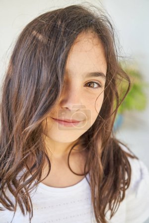 Téléchargez les photos : Portrait d'adorable fille préadolescente aux longs cheveux foncés et aux yeux bruns en t-shirt blanc regardant la caméra - en image libre de droit