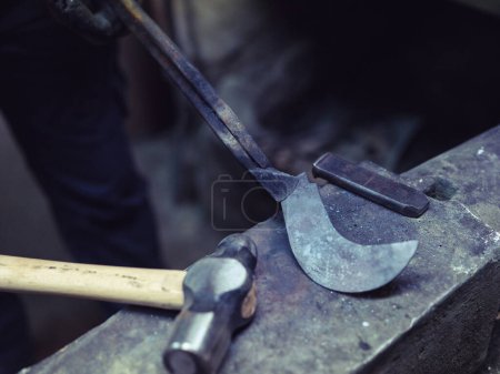 Photo for High angle of crop anonymous male farrier demonstrating metal piece placed on anvil in shabby smithy - Royalty Free Image